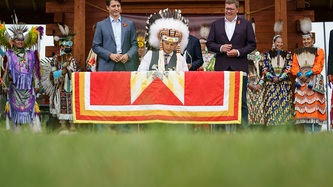 Le chef Delorme de la Nation Cowessess est assis à une table et les PM Trudeau et Moe le regardent