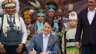 PM Trudeau holds a pen at a table, First Nation people are in focus as they look on 