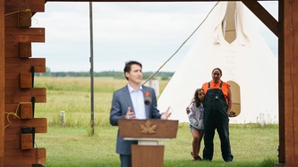 An adult and child look on as Prime Minister Justin Trudeau motions with his hands at a podium