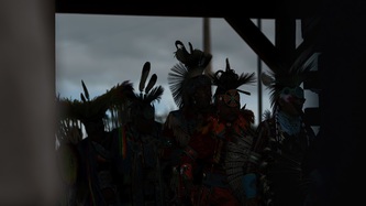 Shadows of Cowessess First Nation people in ceremonial attire against a cloudy sky.
