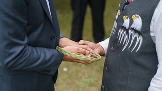 Two men stand holding a braided item together