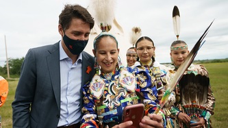 Cowessess First Nation women stand near Prime Minister Trudeau with one holding a phone 