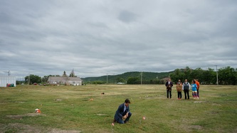 Prime Minister Justin Trudeau kneels in grass near a solar light and small pink flag in the ground