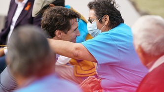 A woman extends her arm as Prime Minister Justin Trudeau kneels and holds her hand