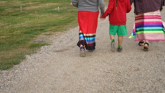 Three people holding hands walk on a gravel path