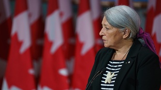 Mme Mary Simon est au micro devant une série de drapeaux canadiens