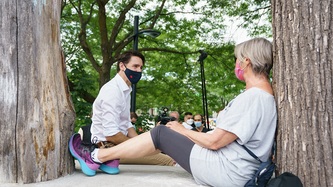PM Trudeau sits and talks to a woman resting against a tree