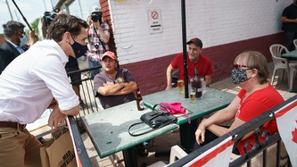 Prime Minister Trudeau stops on a sidewalk to talk with citizens sitting on a patio