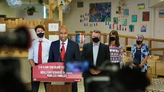 Minister Hussen stands at a podium with PM Trudeau and others behind him
