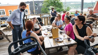 Le PM Trudeau debout près de femmes et de bébés qui rient à la table d’un restaurant