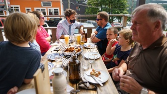 PM Trudeau and a man look to one another at the end of a table seated with people at an eatery