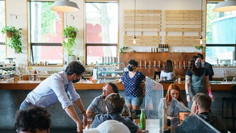Le PM Trudeau s’appuie sur une table sous le regard d’un homme qui sourit