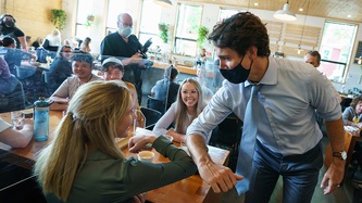 PM Trudeau and a woman at a table exchange an elbow bump as others look on smiling