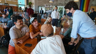 Le PM Trudeau adossé à une chaise à une table avec des gens qui sourient