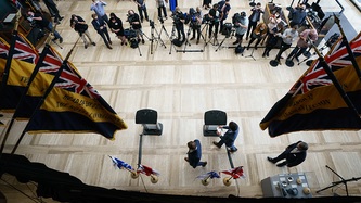 A bird’s eye view of a media availability room with media and technicians with their gear