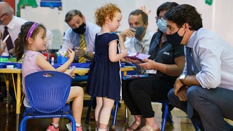 PM Trudeau is hunched down at eye level with a little girl near a small table