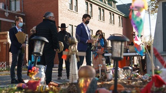 A multitude of flowers and candles lay on the ground as PM Trudeau motions forward holding flowers