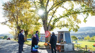 Sun beams through a large tree, PM Trudeau, Minister Miller and others face an engraved monument