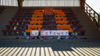 Children's boots and shoes stand atop empty orange benches; signs read 215, and "the missing"