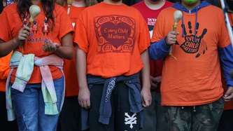 Three children stand wearing orange "every child matters" t-shirts