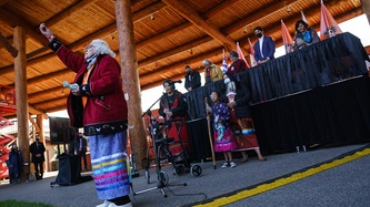 A woman stands on a stage with an arm towards the sky