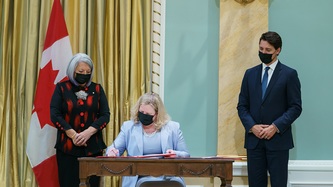 Janice Charette signe un document sous les regards de la GG Mary Simon et du PM Trudeau
