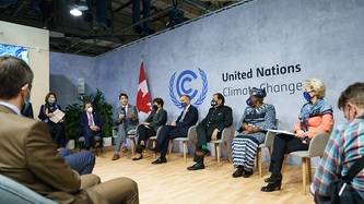 Prime Minister Justin Trudeau and others sit in front of a large scale UN banner behind them