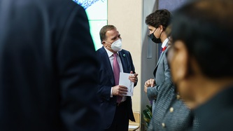 Prime Minister Justin Trudeau stands with others and looks at a man holding paper