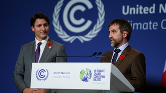 Minister Steven Guilbeault stands at a podium as Prime Minister Justin Trudeau looks on