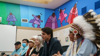 Des œuvres d'art autochtones sont peintes sur le mur. À l’avant-plan, le PM Trudeau et la ministre Hajdu sont assis avec des dirigeants autochtones