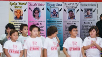 Memorial banners of victims on a wall. In the foreground, children are standing.