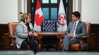 Le PM Trudeau est assis et discute avec la cheffe RoseAnne Archibald