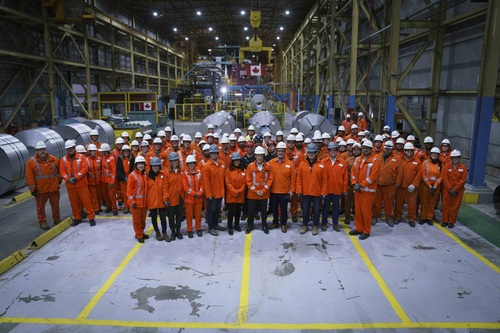 Prime Minister-designate Mark Carney standing with Ministers and ArcelorMittal Dofasco workers at a steel plant.