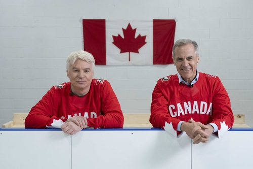 Prime Minister Mark Carney and Mike Myers leaning on the boards of an ice rink. They are wearing Canadian hockey jerseys.