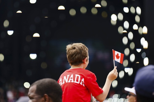 A boy wearing a red Canada shirt is waving a mini Canadian flag.
