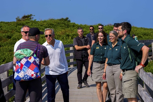 Prime Minister Mark Carney shakes hands with a man, as Parks Canada employees and others look on at PEI National Park.