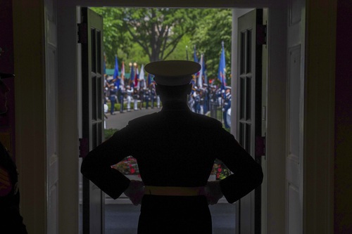 A silhouette of a guard standing at an open door at the White House. Other guards stand outside in the background.