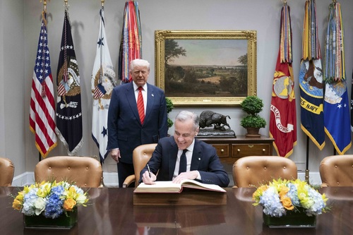 Prime Minister Carney signs the White House guest book. President Trump is standing behind him.