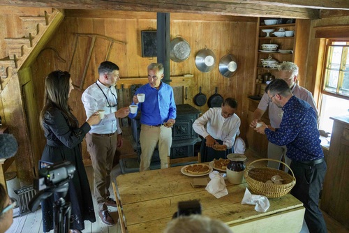 Prime Minister Mark Carney standing with people in a house at the Village Historique Acadien. They are all drinking coffee.