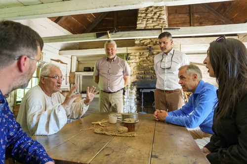 Prime Minister Mark Carney sits at a table and talks with people inside a house at the Village Historique 