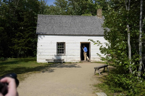Prime Minister Mark Carney stands inside a house while holding a broom at the Village Historique Acadien.