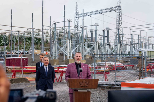 Mayor Sean Bujtas delivers remarks at a podium to introduce Prime Minister Mark Carney and Minister Gregor Robertson befor...