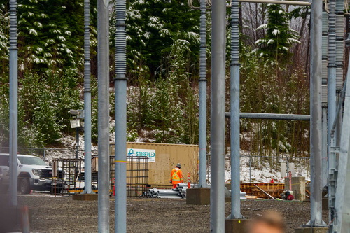A worker in an orange vest walks past a shipping container and construction materials on the grounds of the BC Hydro Skeen...
