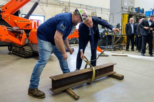 Le premier ministre Mark Carney enroule une sangle de levage autour d'une pièce métallique tandis qu'un travailleur se tie...