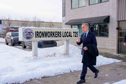 Le premier ministre Mark Carney lève le pouce en marchant à l’extérieur devant l’enseigne de la section locale 725 du synd...